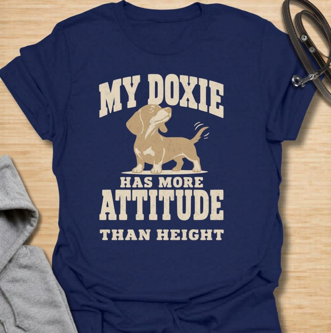 A funny dachshund T-shirt for anyone who knows these little dogs make up for their short legs with an enormous personality. Featuring the phrase “My Doxie Has More Attitude Than Height” with a confident dachshund graphic, this design captures the breed’s bold, stubborn charm perfectly. Ideal for dachshund moms, dachshund dads, sausage dog owners, and anyone who lives with a small dog who thinks big. A playful everyday tee for fans of dachshund humor, doxie attitude, and breed-specific dog gifts.