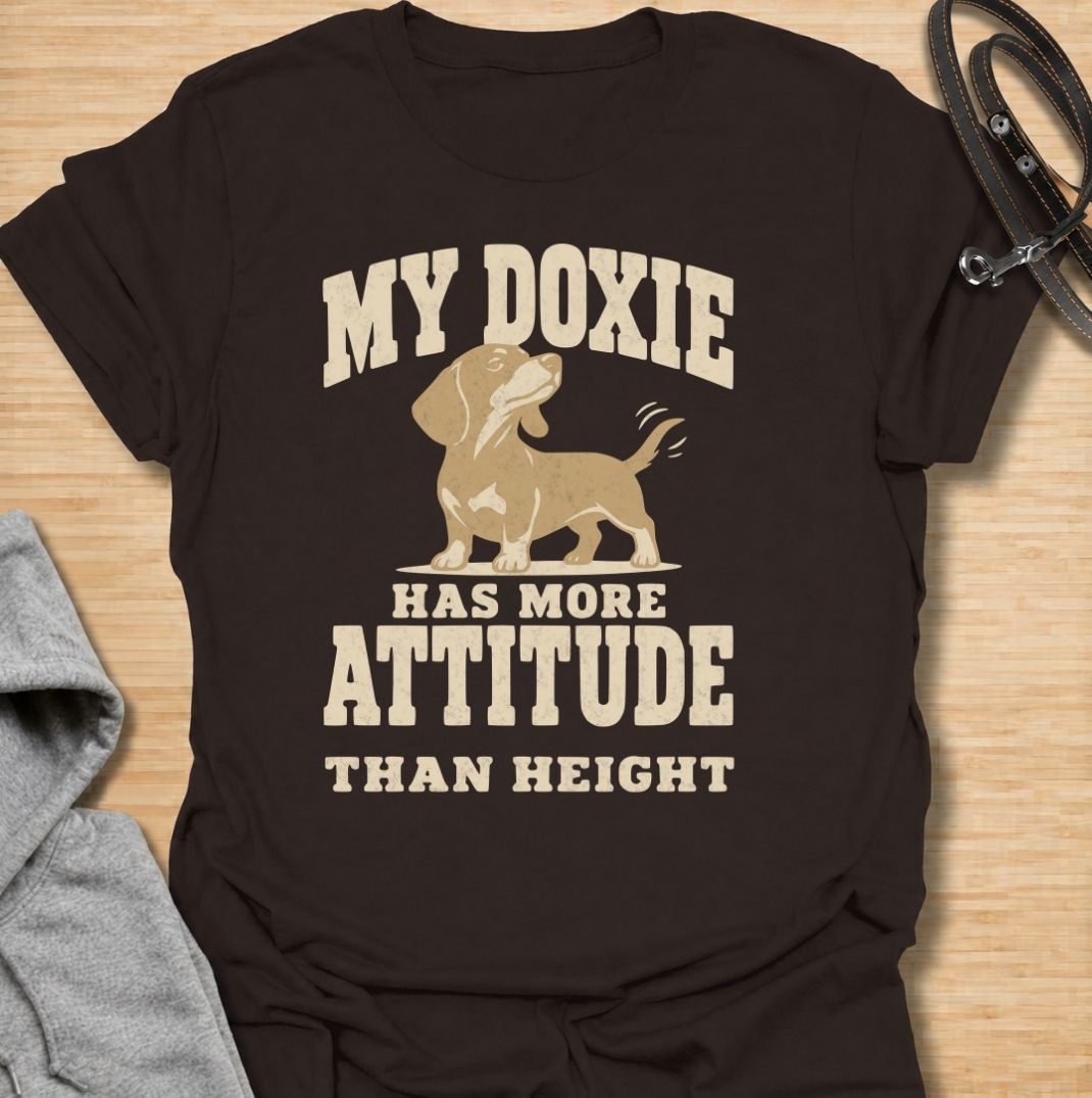 A funny dachshund T-shirt for anyone who knows these little dogs make up for their short legs with an enormous personality. Featuring the phrase “My Doxie Has More Attitude Than Height” with a confident dachshund graphic, this design captures the breed’s bold, stubborn charm perfectly. Ideal for dachshund moms, dachshund dads, sausage dog owners, and anyone who lives with a small dog who thinks big. A playful everyday tee for fans of dachshund humor, doxie attitude, and breed-specific dog gifts.
