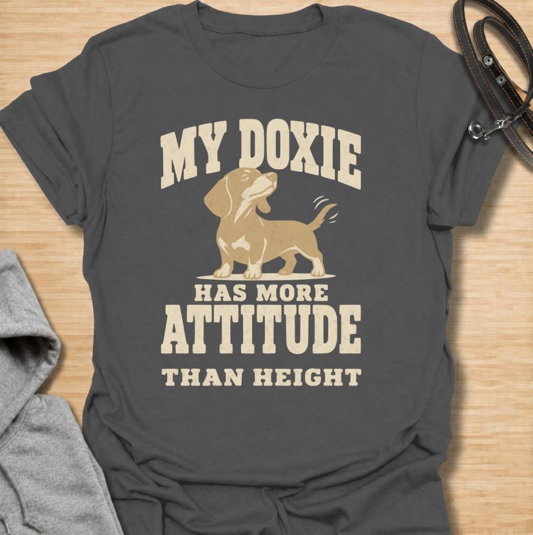 A funny dachshund T-shirt for anyone who knows these little dogs make up for their short legs with an enormous personality. Featuring the phrase “My Doxie Has More Attitude Than Height” with a confident dachshund graphic, this design captures the breed’s bold, stubborn charm perfectly. Ideal for dachshund moms, dachshund dads, sausage dog owners, and anyone who lives with a small dog who thinks big. A playful everyday tee for fans of dachshund humor, doxie attitude, and breed-specific dog gifts.