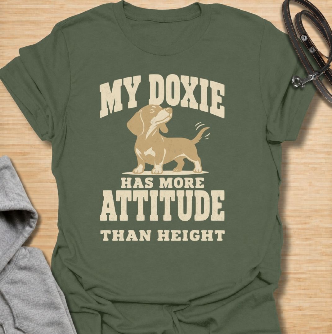 A funny dachshund T-shirt for anyone who knows these little dogs make up for their short legs with an enormous personality. Featuring the phrase “My Doxie Has More Attitude Than Height” with a confident dachshund graphic, this design captures the breed’s bold, stubborn charm perfectly. Ideal for dachshund moms, dachshund dads, sausage dog owners, and anyone who lives with a small dog who thinks big. A playful everyday tee for fans of dachshund humor, doxie attitude, and breed-specific dog gifts.