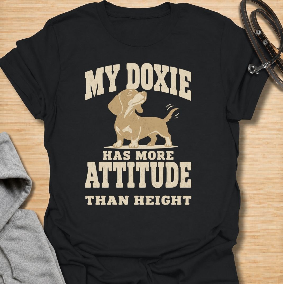 A funny dachshund T-shirt for anyone who knows these little dogs make up for their short legs with an enormous personality. Featuring the phrase “My Doxie Has More Attitude Than Height” with a confident dachshund graphic, this design captures the breed’s bold, stubborn charm perfectly. Ideal for dachshund moms, dachshund dads, sausage dog owners, and anyone who lives with a small dog who thinks big. A playful everyday tee for fans of dachshund humor, doxie attitude, and breed-specific dog gifts.