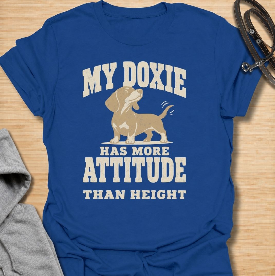 A funny dachshund T-shirt for anyone who knows these little dogs make up for their short legs with an enormous personality. Featuring the phrase “My Doxie Has More Attitude Than Height” with a confident dachshund graphic, this design captures the breed’s bold, stubborn charm perfectly. Ideal for dachshund moms, dachshund dads, sausage dog owners, and anyone who lives with a small dog who thinks big. A playful everyday tee for fans of dachshund humor, doxie attitude, and breed-specific dog gifts.