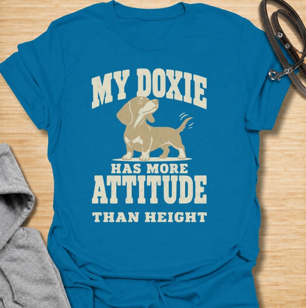 A funny dachshund T-shirt for anyone who knows these little dogs make up for their short legs with an enormous personality. Featuring the phrase “My Doxie Has More Attitude Than Height” with a confident dachshund graphic, this design captures the breed’s bold, stubborn charm perfectly. Ideal for dachshund moms, dachshund dads, sausage dog owners, and anyone who lives with a small dog who thinks big. A playful everyday tee for fans of dachshund humor, doxie attitude, and breed-specific dog gifts.