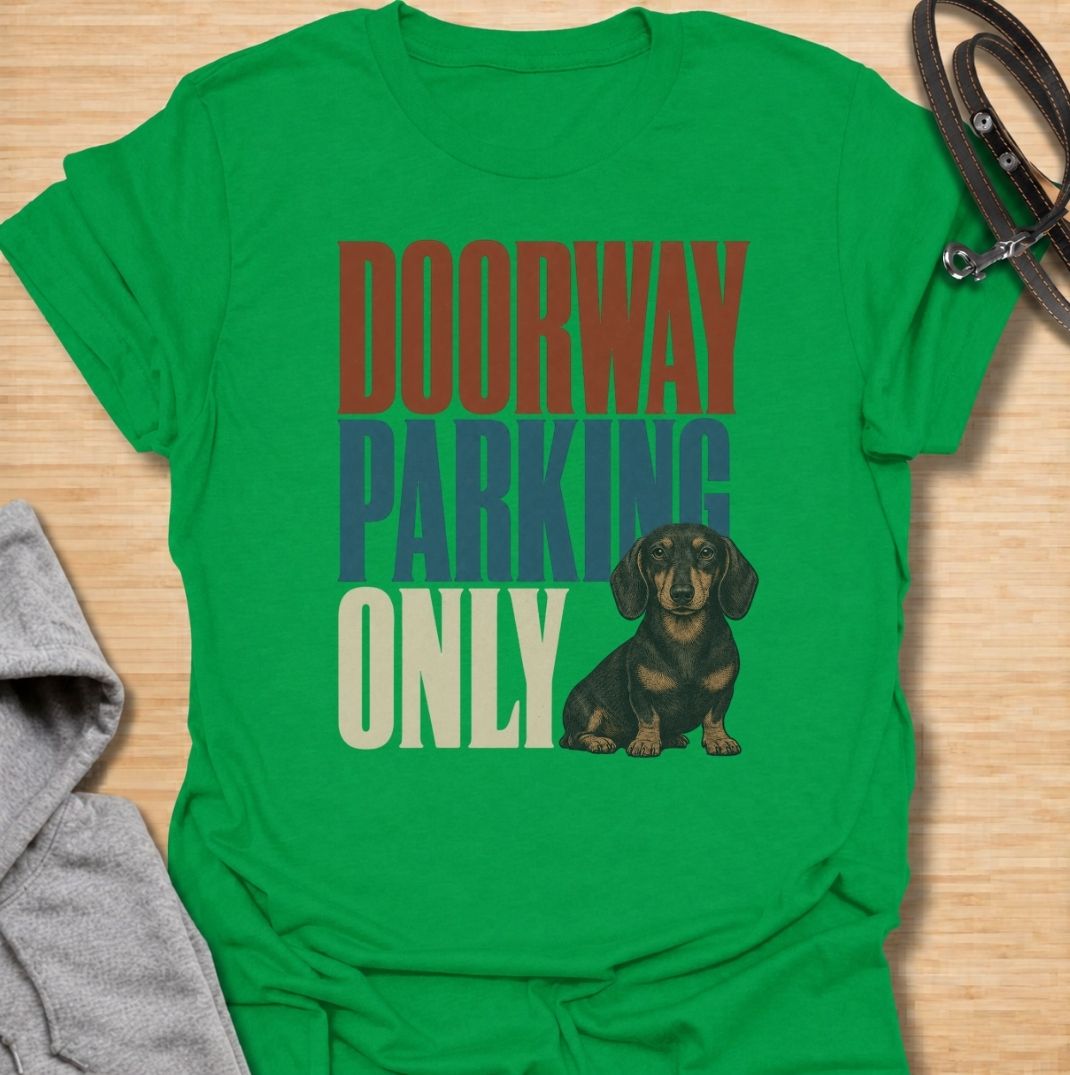 A funny dachshund T-shirt for anyone who knows these little dogs have a talent for stopping exactly where you need to walk. Featuring the phrase “Doorway Parking Only” with a seated dachshund graphic, this design captures one of those everyday breed habits owners instantly recognize. Perfect for dachshund moms, dachshund dads, sausage dog owners, and anyone who regularly finds their path blocked by a very small dog. A playful everyday tee for fans of dachshund humor, doxies, and breed-specific dog gifts.