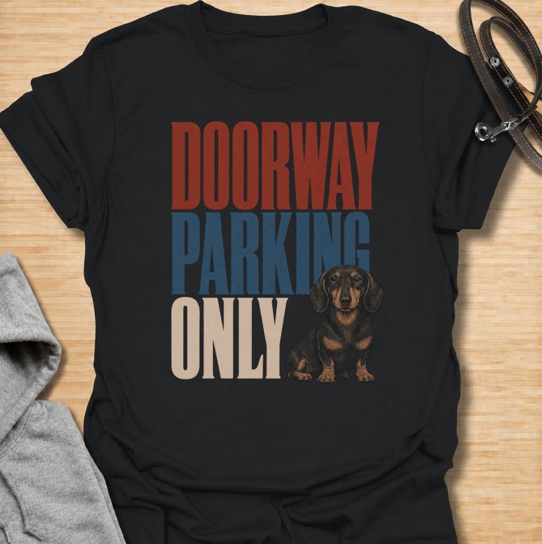A funny dachshund T-shirt for anyone who knows these little dogs have a talent for stopping exactly where you need to walk. Featuring the phrase “Doorway Parking Only” with a seated dachshund graphic, this design captures one of those everyday breed habits owners instantly recognize. Perfect for dachshund moms, dachshund dads, sausage dog owners, and anyone who regularly finds their path blocked by a very small dog. A playful everyday tee for fans of dachshund humor, doxies, and breed-specific dog gifts.