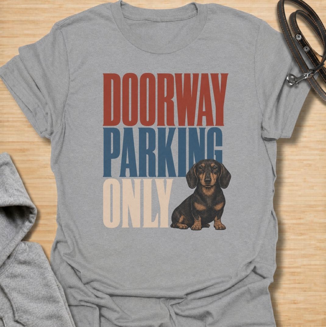 A funny dachshund T-shirt for anyone who knows these little dogs have a talent for stopping exactly where you need to walk. Featuring the phrase “Doorway Parking Only” with a seated dachshund graphic, this design captures one of those everyday breed habits owners instantly recognize. Perfect for dachshund moms, dachshund dads, sausage dog owners, and anyone who regularly finds their path blocked by a very small dog. A playful everyday tee for fans of dachshund humor, doxies, and breed-specific dog gifts.