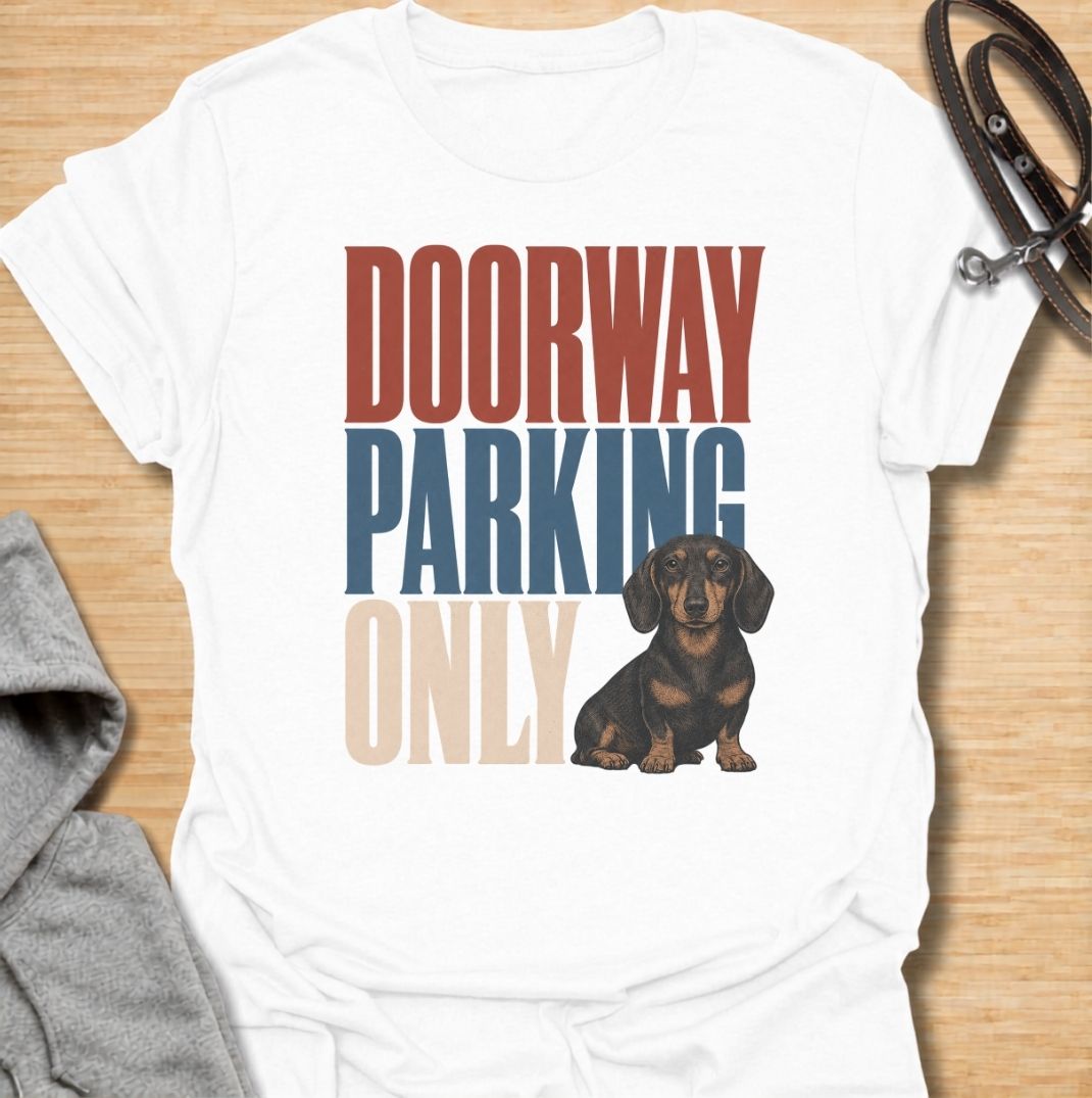 A funny dachshund T-shirt for anyone who knows these little dogs have a talent for stopping exactly where you need to walk. Featuring the phrase “Doorway Parking Only” with a seated dachshund graphic, this design captures one of those everyday breed habits owners instantly recognize. Perfect for dachshund moms, dachshund dads, sausage dog owners, and anyone who regularly finds their path blocked by a very small dog. A playful everyday tee for fans of dachshund humor, doxies, and breed-specific dog gifts.