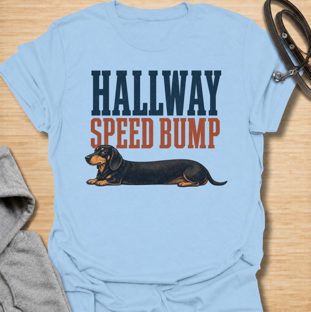 A funny dachshund T-shirt for anyone who knows the hallway is rarely clear when a sausage dog is around. Featuring the phrase “Hallway Speed Bump” with a dachshund stretched out across the floor, this design turns a familiar breed habit into a dry visual joke. Perfect for dachshund moms, dachshund dads, wiener dog owners, and anyone who regularly has to step over their dog at home. A playful everyday tee for fans of dachshund humor, long dogs, and breed-specific dog gifts.