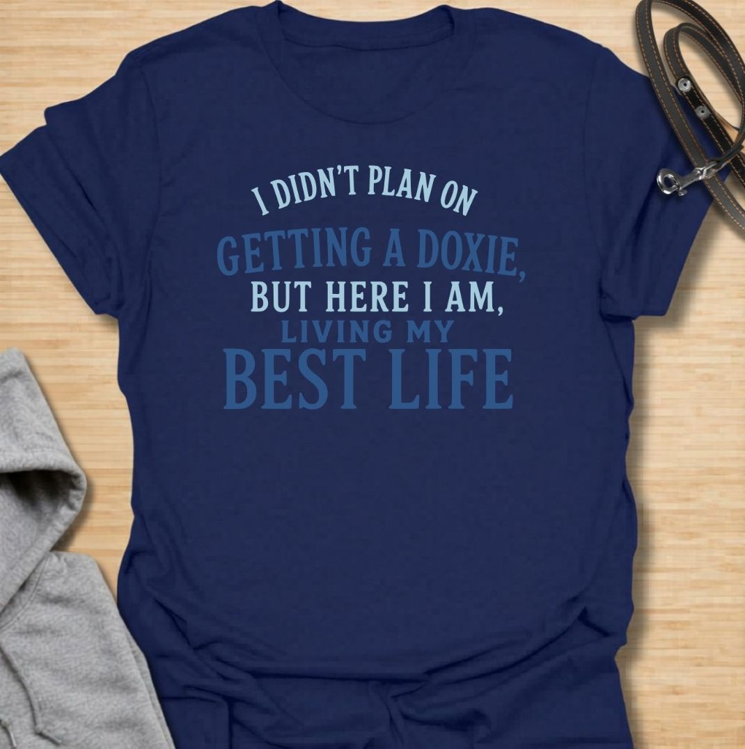 A funny dachshund T-shirt for anyone who never planned on becoming a doxie person but somehow ended up completely devoted. Featuring the phrase “I Didn’t Plan on Getting a Doxie, But Here I Am, Living My Best Life,” this text-based design captures the happy reality of dachshund ownership. Perfect for dachshund moms, dachshund dads, new doxie owners, and anyone who fell unexpectedly in love with the breed. A warm, relatable everyday tee for fans of dachshund humor, sausage dogs, and breed-specific gifts.