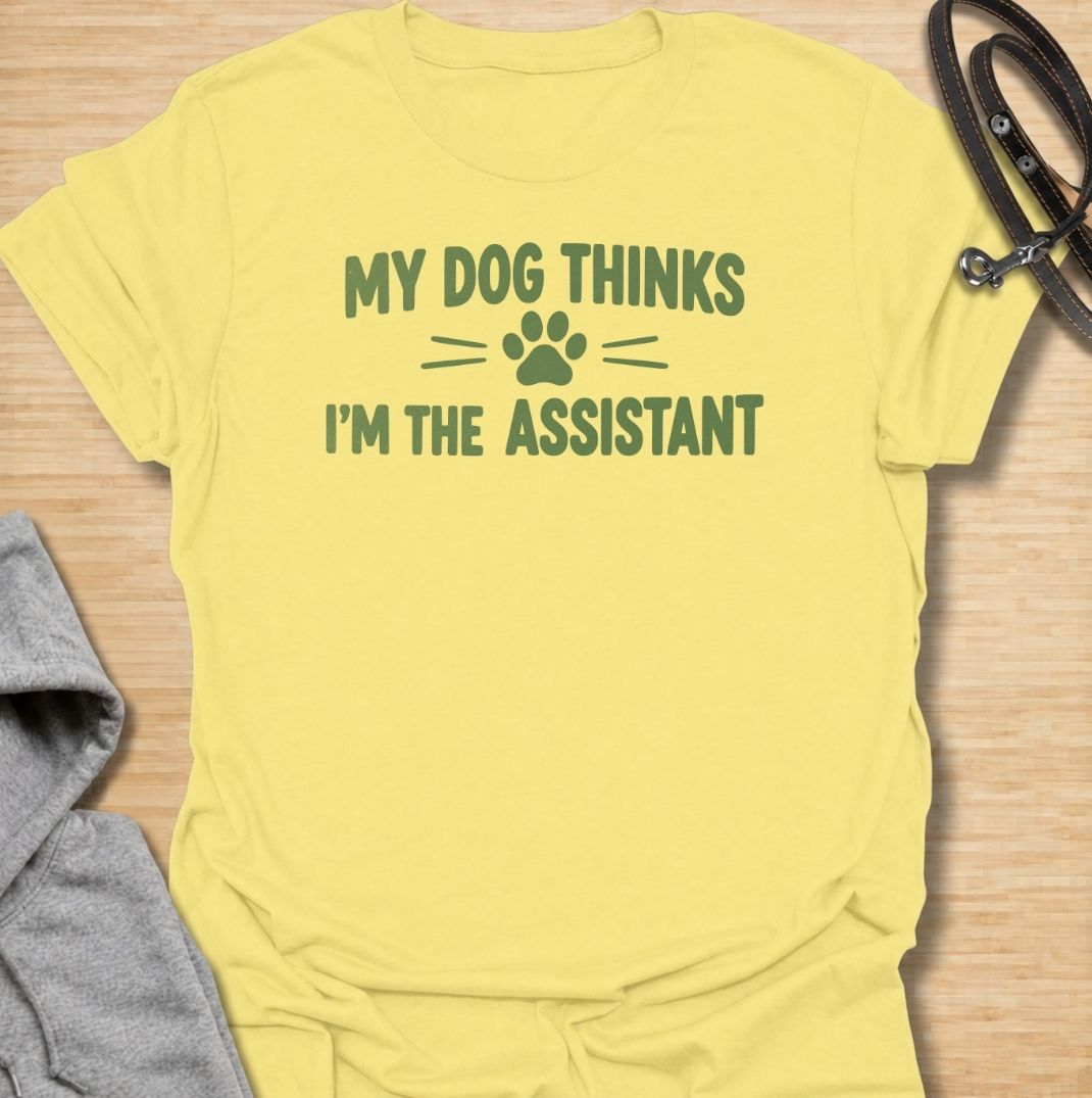 A funny dog T-shirt for anyone who knows their dog is really the one running the household. Featuring the phrase “My Dog Thinks I’m the Assistant” with a simple paw print graphic, this clean text-based design captures everyday dog-owner life with relatable humor. Perfect for dog moms, dog dads, rescue dog owners, and anyone whose pet expects first-class service at all times. A playful everyday tee for fans of funny dog sayings, pet parent humor, and general dog lover gifts.