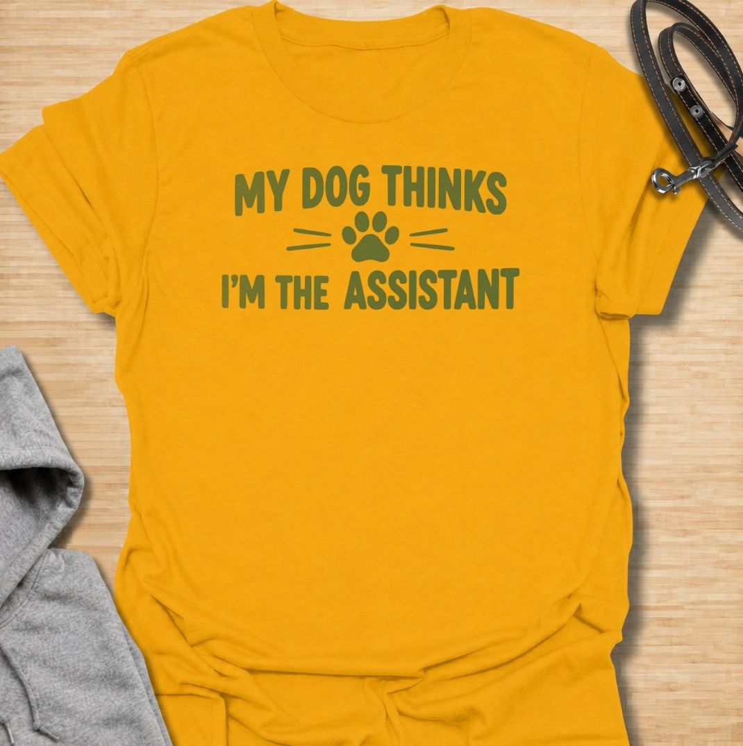A funny dog T-shirt for anyone who knows their dog is really the one running the household. Featuring the phrase “My Dog Thinks I’m the Assistant” with a simple paw print graphic, this clean text-based design captures everyday dog-owner life with relatable humor. Perfect for dog moms, dog dads, rescue dog owners, and anyone whose pet expects first-class service at all times. A playful everyday tee for fans of funny dog sayings, pet parent humor, and general dog lover gifts.