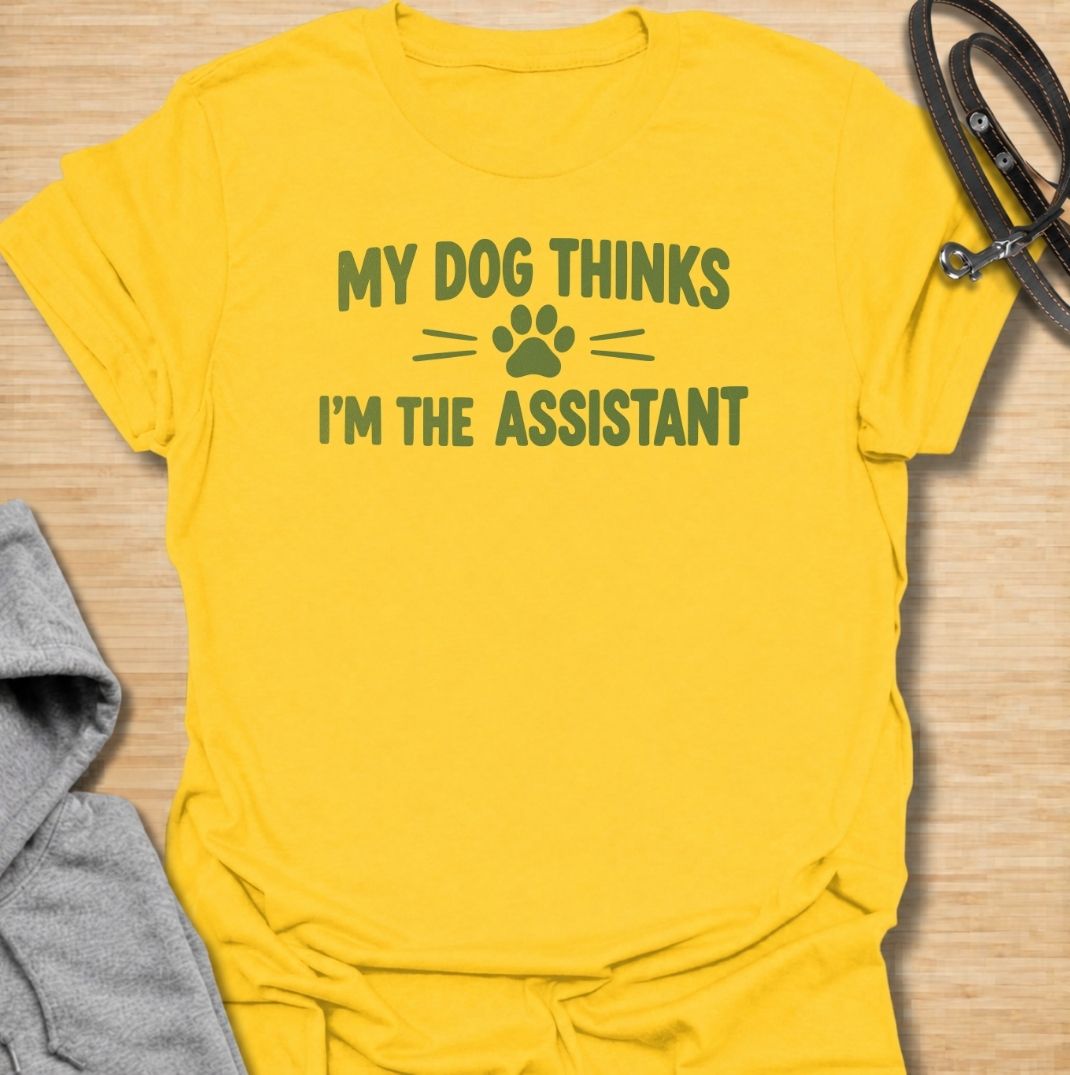 A funny dog T-shirt for anyone who knows their dog is really the one running the household. Featuring the phrase “My Dog Thinks I’m the Assistant” with a simple paw print graphic, this clean text-based design captures everyday dog-owner life with relatable humor. Perfect for dog moms, dog dads, rescue dog owners, and anyone whose pet expects first-class service at all times. A playful everyday tee for fans of funny dog sayings, pet parent humor, and general dog lover gifts.
