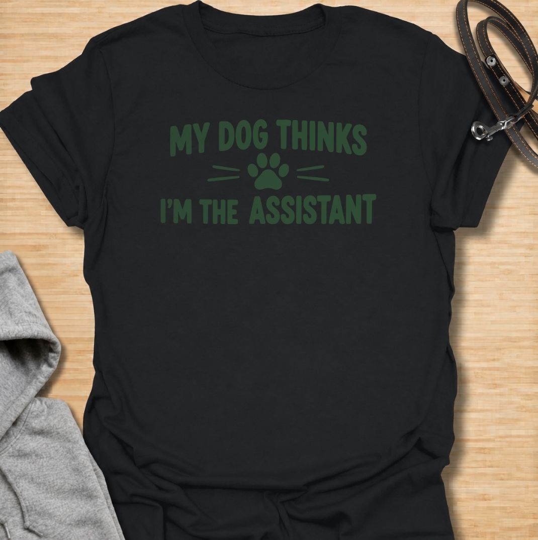 A funny dog T-shirt for anyone who knows their dog is really the one running the household. Featuring the phrase “My Dog Thinks I’m the Assistant” with a simple paw print graphic, this clean text-based design captures everyday dog-owner life with relatable humor. Perfect for dog moms, dog dads, rescue dog owners, and anyone whose pet expects first-class service at all times. A playful everyday tee for fans of funny dog sayings, pet parent humor, and general dog lover gifts.