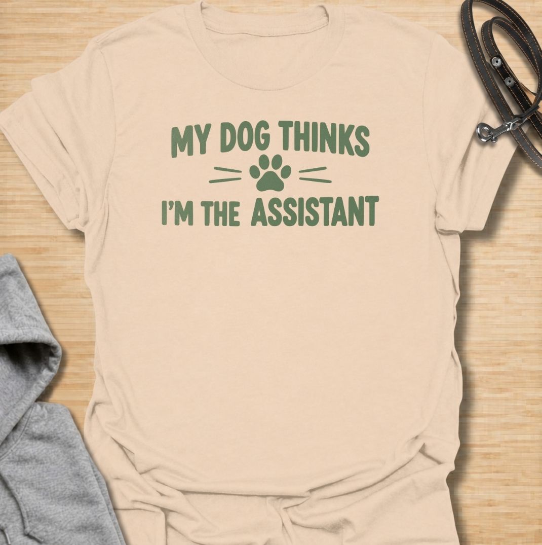 A funny dog T-shirt for anyone who knows their dog is really the one running the household. Featuring the phrase “My Dog Thinks I’m the Assistant” with a simple paw print graphic, this clean text-based design captures everyday dog-owner life with relatable humor. Perfect for dog moms, dog dads, rescue dog owners, and anyone whose pet expects first-class service at all times. A playful everyday tee for fans of funny dog sayings, pet parent humor, and general dog lover gifts.