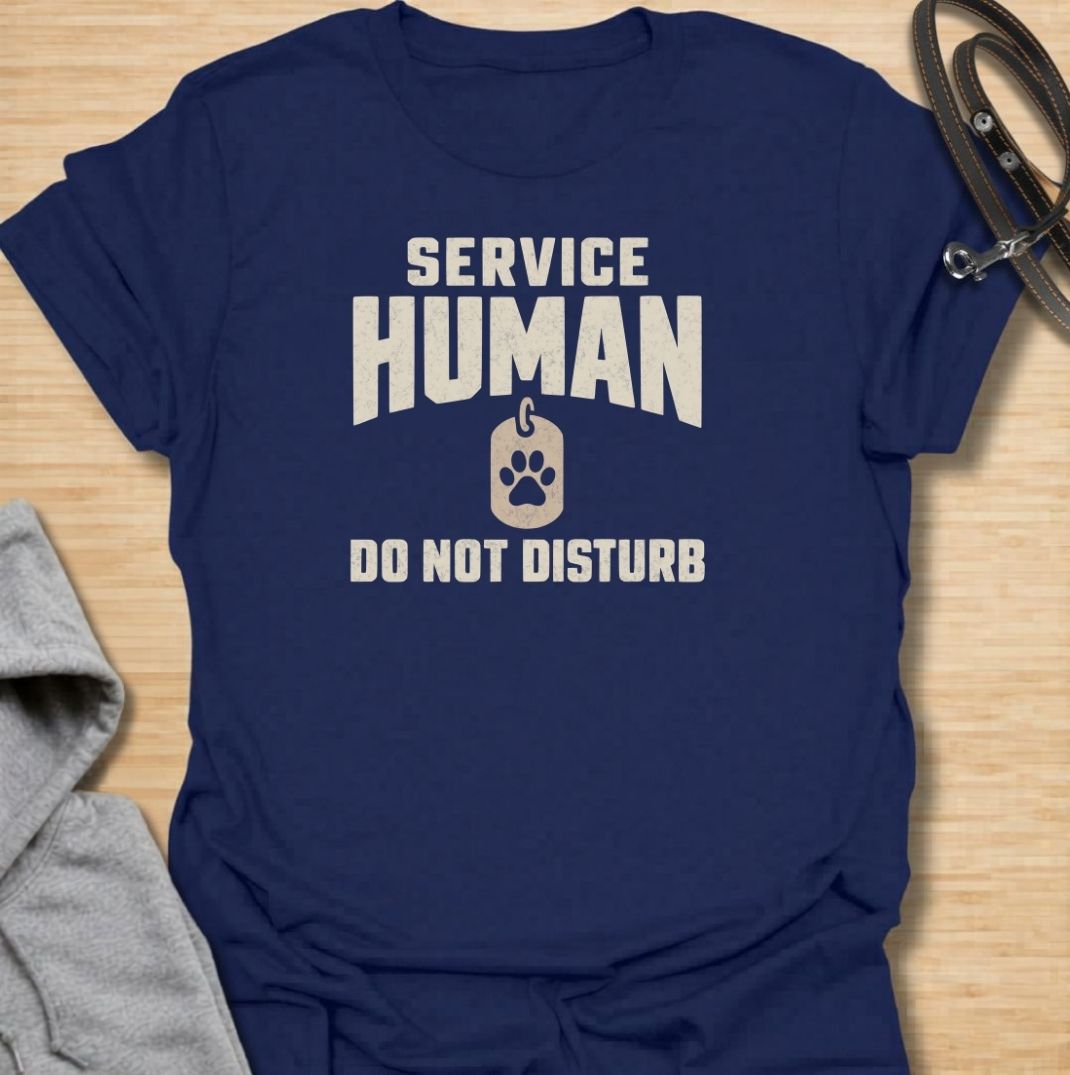 A funny dog T-shirt for anyone who knows their main role at home is serving the dog. Featuring the phrase “Service Human — Do Not Disturb” with a simple paw-print tag graphic, this clean design turns the service-dog idea on its head with dry pet-owner humor. Perfect for dog moms, dog dads, rescue dog owners, and anyone whose four-legged boss expects constant attention. A playful everyday tee for fans of funny dog sayings, pet parent humor, and general dog lover gifts.