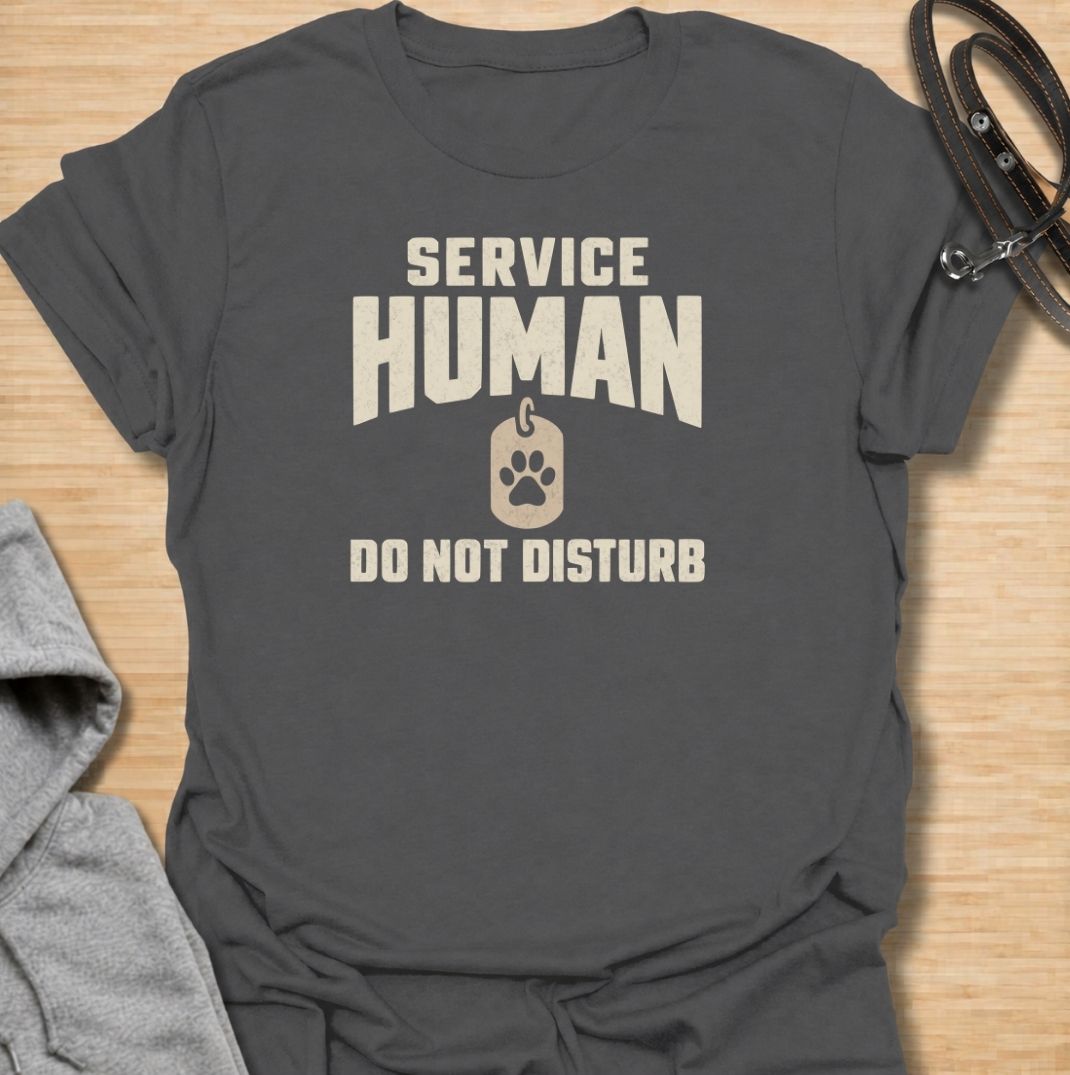 A funny dog T-shirt for anyone who knows their main role at home is serving the dog. Featuring the phrase “Service Human — Do Not Disturb” with a simple paw-print tag graphic, this clean design turns the service-dog idea on its head with dry pet-owner humor. Perfect for dog moms, dog dads, rescue dog owners, and anyone whose four-legged boss expects constant attention. A playful everyday tee for fans of funny dog sayings, pet parent humor, and general dog lover gifts.