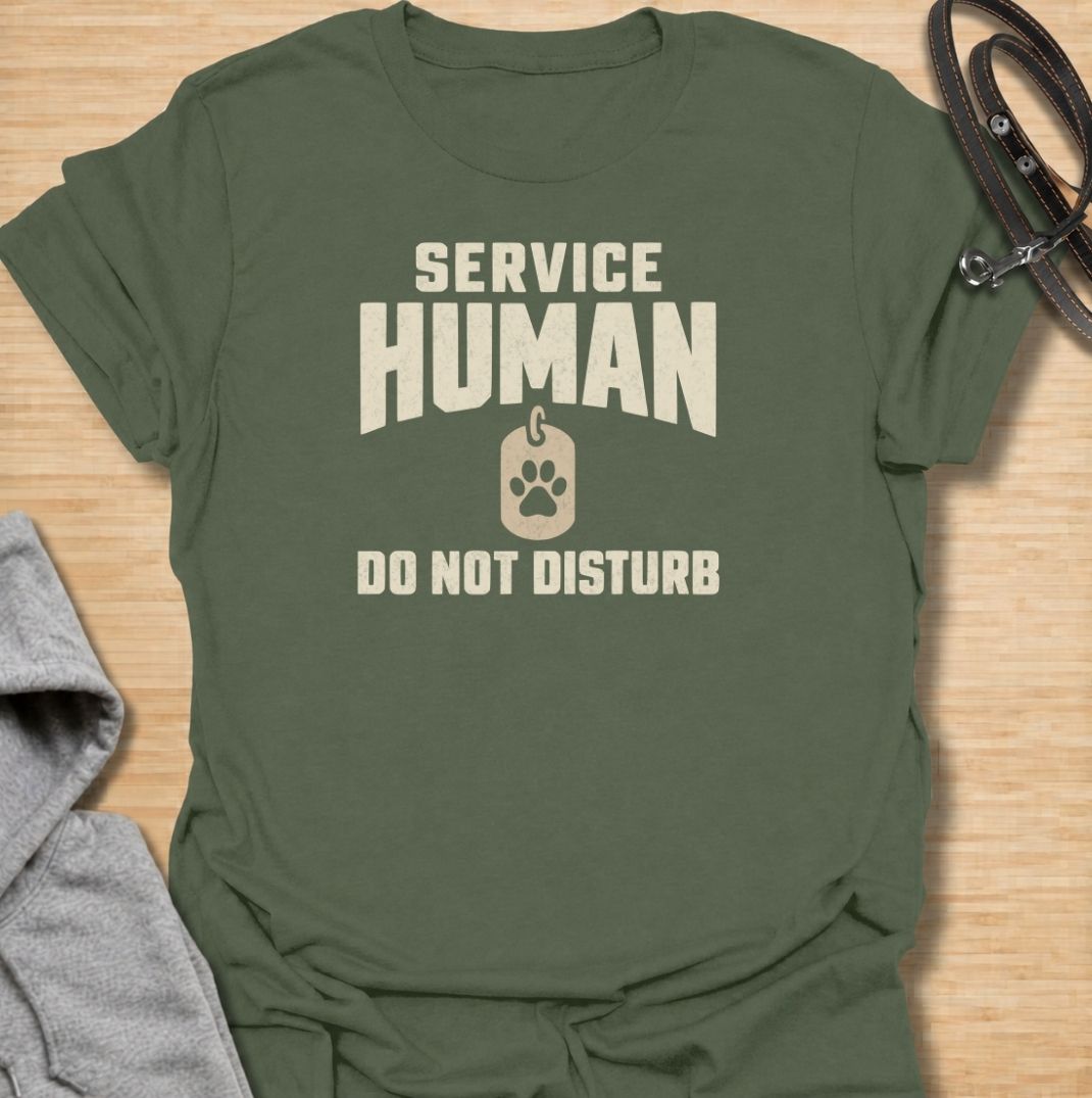 A funny dog T-shirt for anyone who knows their main role at home is serving the dog. Featuring the phrase “Service Human — Do Not Disturb” with a simple paw-print tag graphic, this clean design turns the service-dog idea on its head with dry pet-owner humor. Perfect for dog moms, dog dads, rescue dog owners, and anyone whose four-legged boss expects constant attention. A playful everyday tee for fans of funny dog sayings, pet parent humor, and general dog lover gifts.
