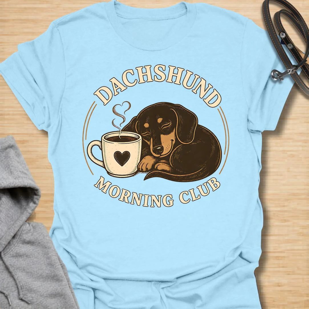 This Dachshund Morning Club t-shirt is made for doxie lovers who know mornings are better with coffee and a little long dog nearby. Featuring a cozy dachshund curled beside a steaming mug with vintage-style circular lettering, this cute dog design is great for dachshund moms, dachshund dads, coffee lovers, wiener dog fans, rescue dog lovers, and anyone whose morning routine includes caffeine and dachshund company.