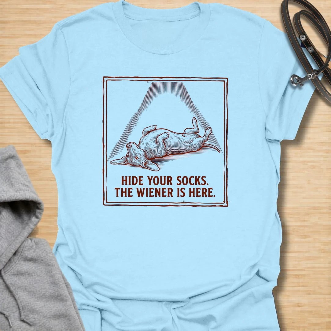 This Hide Your Socks The Wiener Is Here t-shirt is made for dachshund lovers who know their little long dog can turn laundry into a crime scene. Featuring a vintage-style dachshund under a dramatic blanket shape with bold warning text, this design has a funny mischievous dog-parent feel. Perfect for dachshund moms, dachshund dads, wiener dog fans, rescue dog lovers, and anyone whose doxie has a thing for socks.
