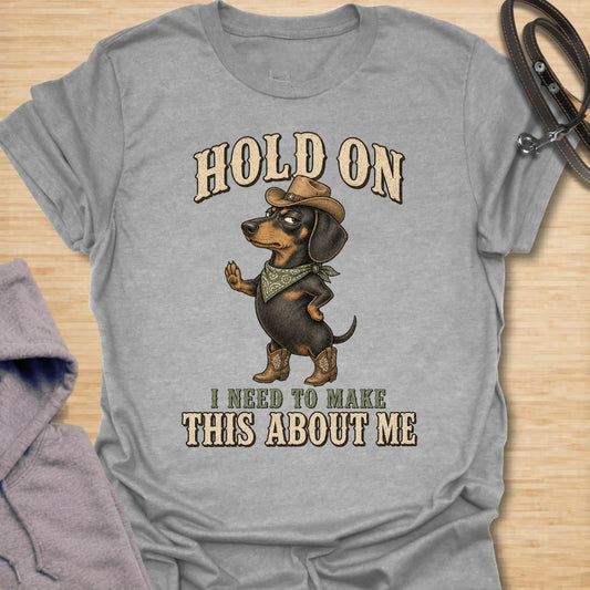 This Hold On I Need To Make This About Me t-shirt is made for dachshund lovers who know their little long dog must be the center of every conversation. Featuring a western-style dachshund in a hat, boots, and bandana with bold vintage lettering, this design has a funny main-character dog-parent feel. Perfect for dachshund moms, dachshund dads, wiener dog fans, rescue dog lovers, and anyone whose doxie always steals the spotlight.