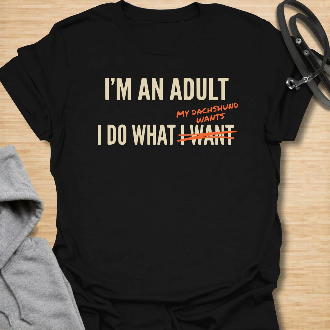 This funny dachshund t-shirt is made for anyone who technically makes their own decisions, but still answers to their doxie. The bold text layout and crossed-out wording give the design a modern, relatable dog parent feel. It is perfect for dachshund moms, doxie dads, and anyone whose little long dog quietly runs the house. A great casual shirt for dog lovers who know adulting mostly means doing what the dachshund wants.