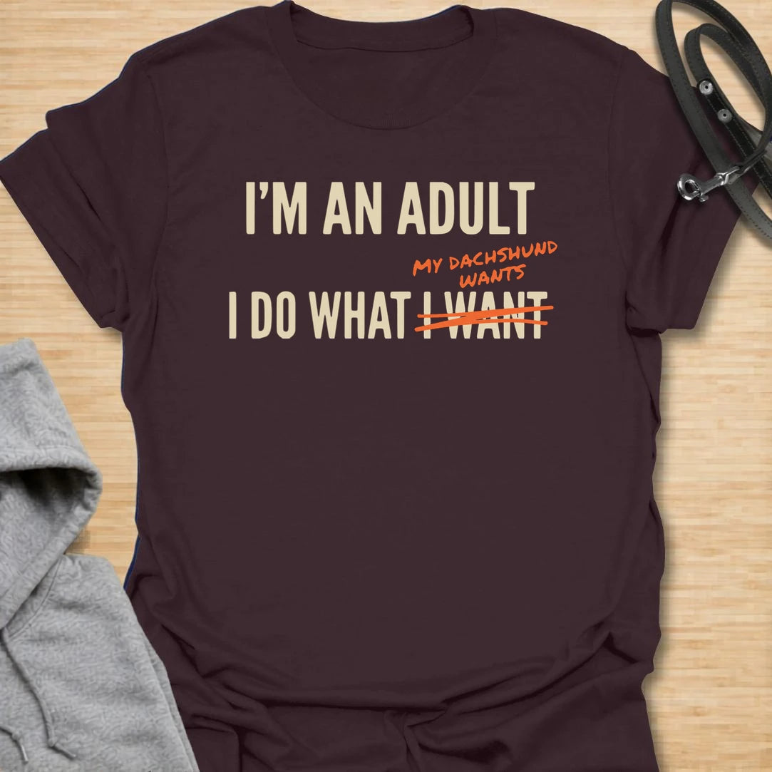 This funny dachshund t-shirt is made for anyone who technically makes their own decisions, but still answers to their doxie. The bold text layout and crossed-out wording give the design a modern, relatable dog parent feel. It is perfect for dachshund moms, doxie dads, and anyone whose little long dog quietly runs the house. A great casual shirt for dog lovers who know adulting mostly means doing what the dachshund wants.