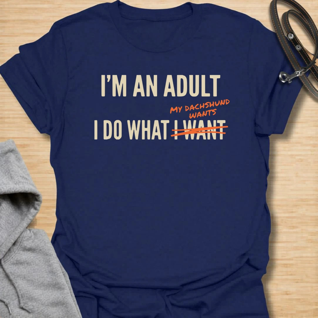 This funny dachshund t-shirt is made for anyone who technically makes their own decisions, but still answers to their doxie. The bold text layout and crossed-out wording give the design a modern, relatable dog parent feel. It is perfect for dachshund moms, doxie dads, and anyone whose little long dog quietly runs the house. A great casual shirt for dog lovers who know adulting mostly means doing what the dachshund wants.