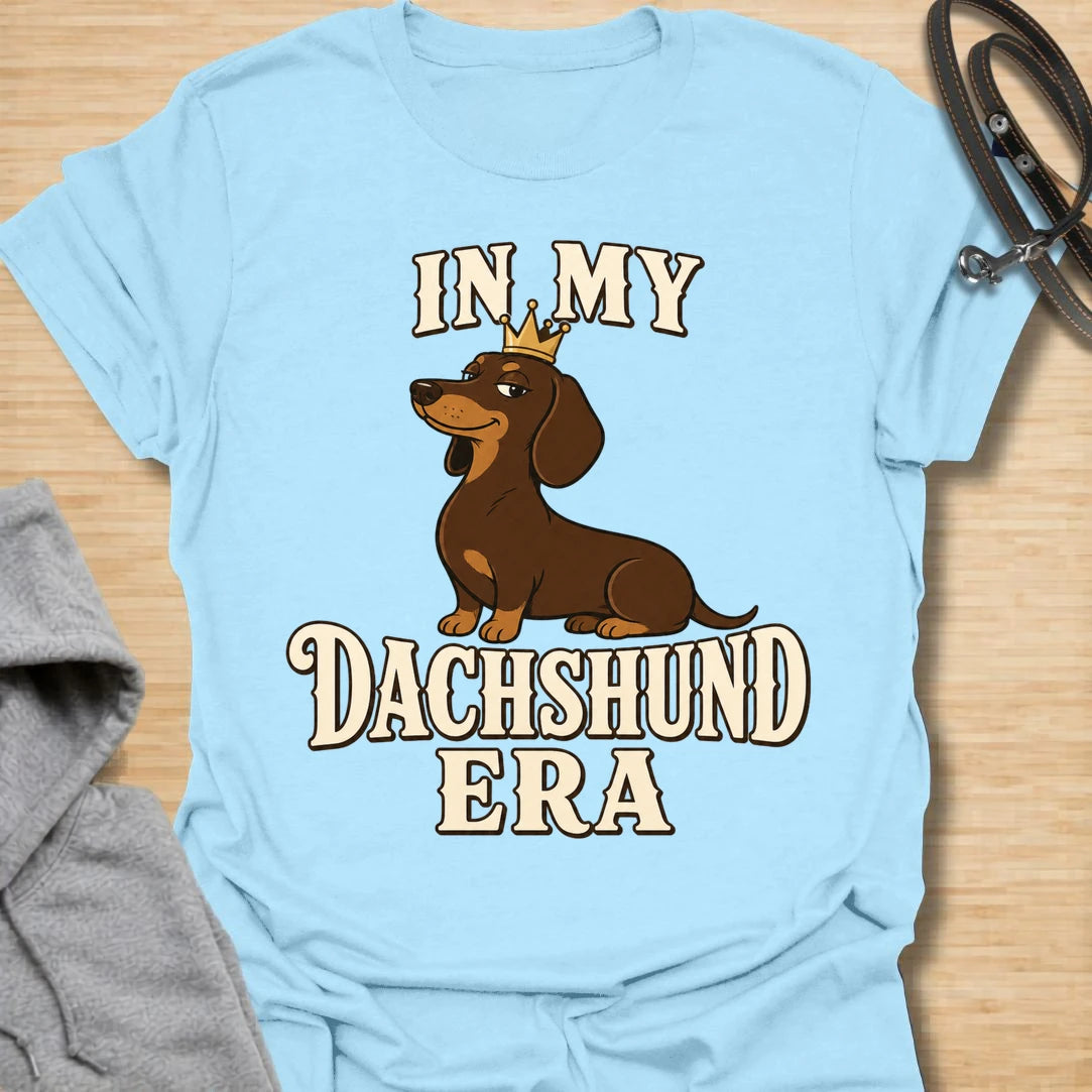 This In My Dachshund Era t-shirt is made for doxie lovers who know their little long dog is not just a pet, it is a whole lifestyle. Featuring a cute dachshund wearing a crown with bold retro-style text, this fun breed-specific design is great for dachshund moms, dachshund dads, wiener dog fans, rescue dog lovers, and anyone proudly living their dachshund era.