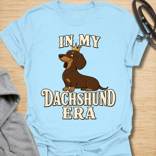 This In My Dachshund Era t-shirt is made for doxie lovers who know their little long dog is not just a pet, it is a whole lifestyle. Featuring a cute dachshund wearing a crown with bold retro-style text, this fun breed-specific design is great for dachshund moms, dachshund dads, wiener dog fans, rescue dog lovers, and anyone proudly living their dachshund era.
