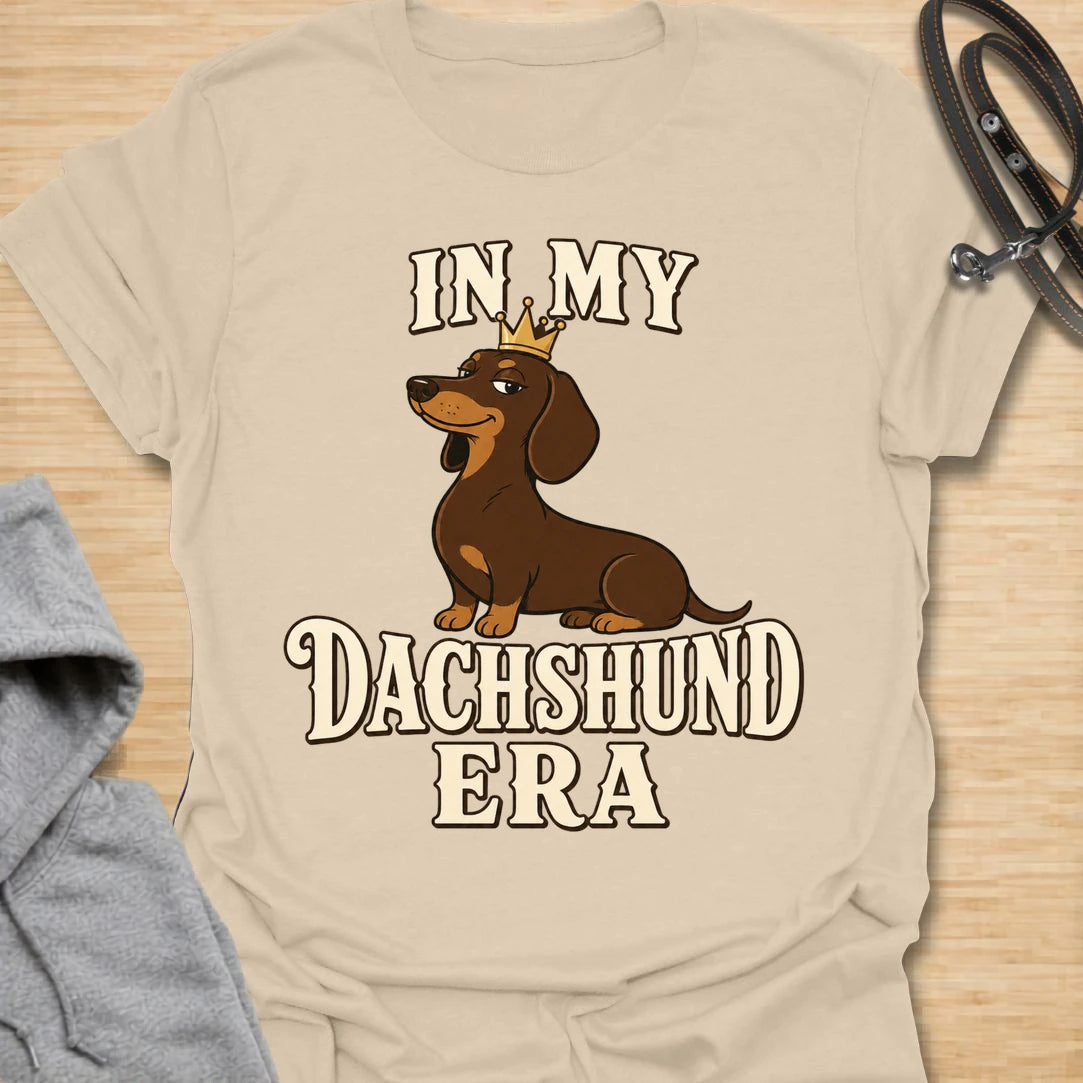 This In My Dachshund Era t-shirt is made for doxie lovers who know their little long dog is not just a pet, it is a whole lifestyle. Featuring a cute dachshund wearing a crown with bold retro-style text, this fun breed-specific design is great for dachshund moms, dachshund dads, wiener dog fans, rescue dog lovers, and anyone proudly living their dachshund era.