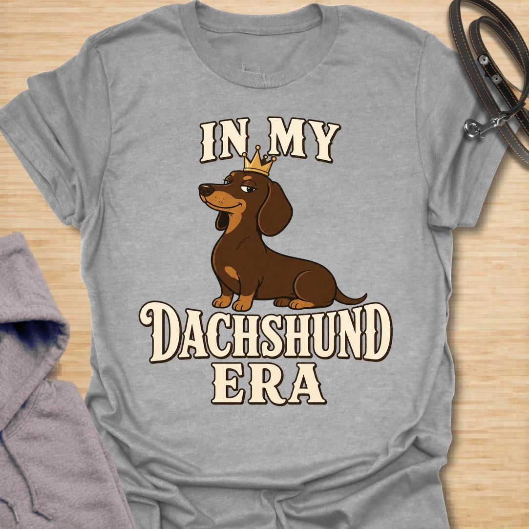 This In My Dachshund Era t-shirt is made for doxie lovers who know their little long dog is not just a pet, it is a whole lifestyle. Featuring a cute dachshund wearing a crown with bold retro-style text, this fun breed-specific design is great for dachshund moms, dachshund dads, wiener dog fans, rescue dog lovers, and anyone proudly living their dachshund era.
