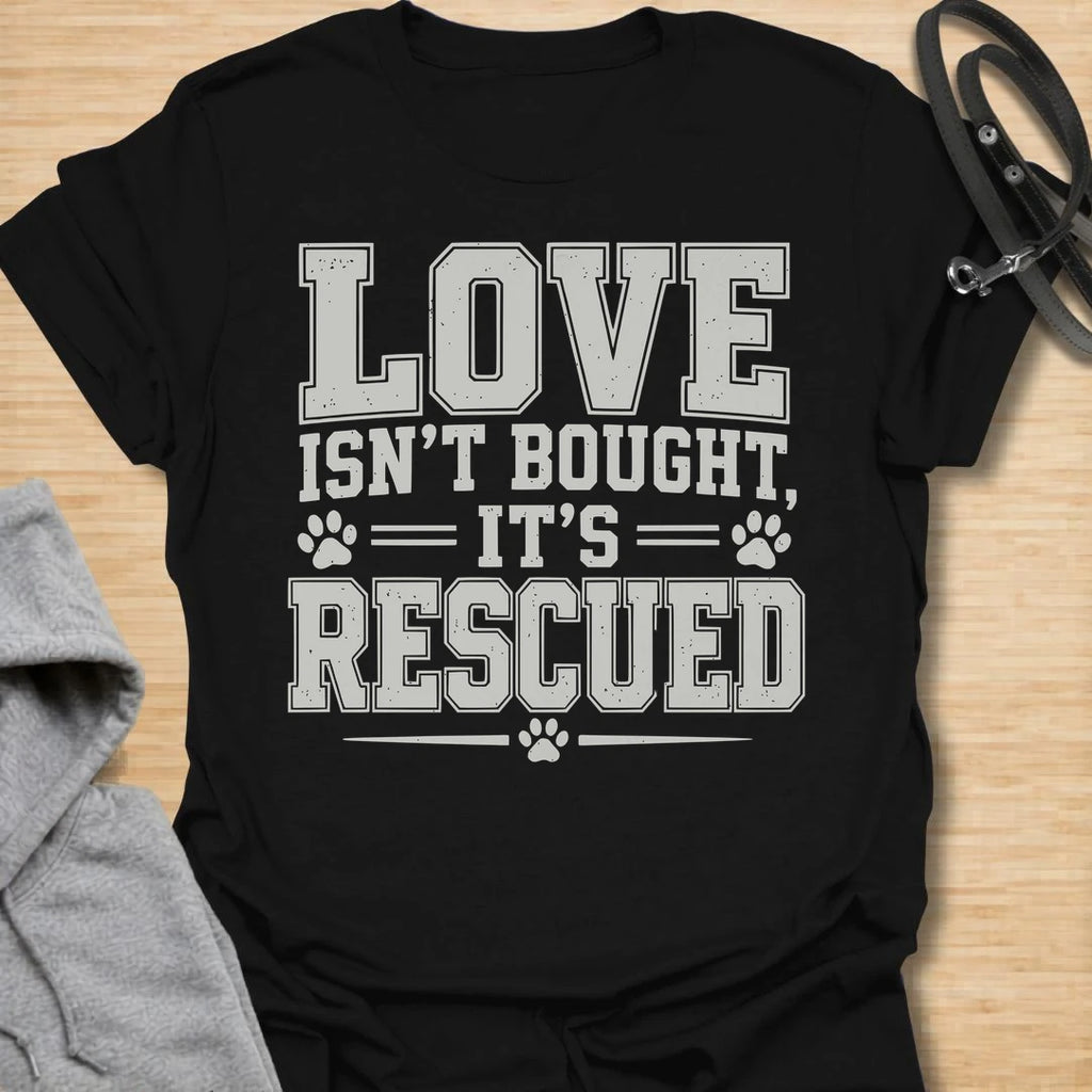 This Love Isn’t Bought, It’s Rescued t-shirt is made for rescue dog lovers who believe the best dogs are found through adoption and second chances. Featuring bold varsity-style lettering with paw print accents, this design has a simple, meaningful rescue-dog message that is easy to wear every day. Perfect for rescue dog moms, rescue dog dads, shelter dog adopters, foster families, animal lovers, and anyone who proudly supports dog rescue. Black