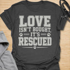 This Love Isn’t Bought, It’s Rescued t-shirt is made for rescue dog lovers who believe the best dogs are found through adoption and second chances. Featuring bold varsity-style lettering with paw print accents, this design has a simple, meaningful rescue-dog message that is easy to wear every day. Perfect for rescue dog moms, rescue dog dads, shelter dog adopters, foster families, animal lovers, and anyone who proudly supports dog rescue. Charcoal