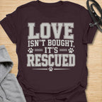 This Love Isn’t Bought, It’s Rescued t-shirt is made for rescue dog lovers who believe the best dogs are found through adoption and second chances. Featuring bold varsity-style lettering with paw print accents, this design has a simple, meaningful rescue-dog message that is easy to wear every day. Perfect for rescue dog moms, rescue dog dads, shelter dog adopters, foster families, animal lovers, and anyone who proudly supports dog rescue. Dark Chocolate