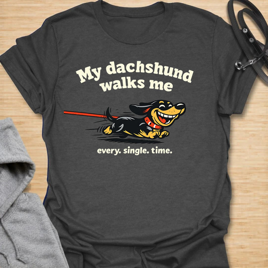 This My Dachshund Walks Me t-shirt is made for dachshund lovers who know who is really in charge of every walk. Featuring a happy running doxie pulling the leash with bold playful lettering and the phrase Every. Single. Time., this design has a funny chaotic dog-parent feel that wiener dog fans will instantly understand. Perfect for dachshund moms, dachshund dads, doxie owners, rescue dog lovers, and anyone whose tiny-legged dog sets the pace.
