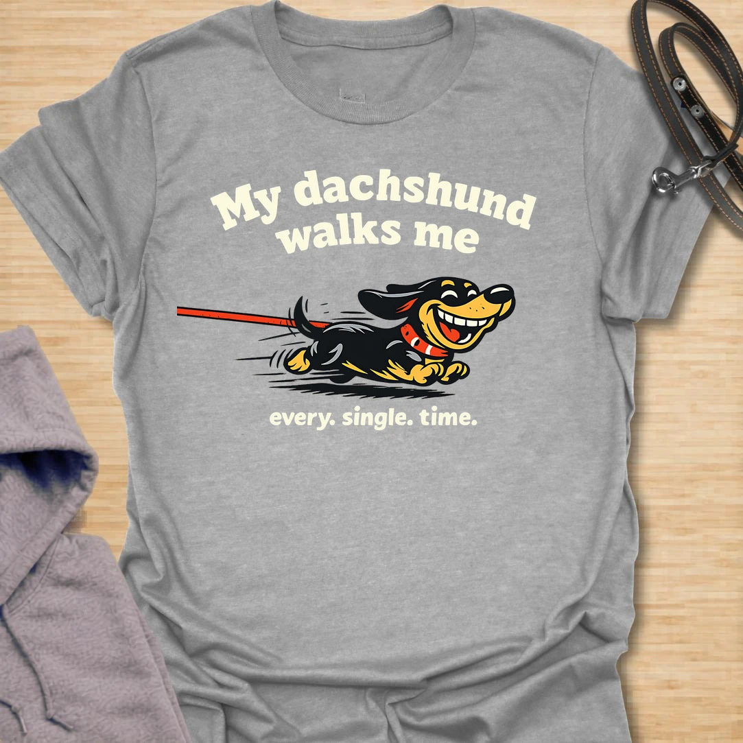 This My Dachshund Walks Me t-shirt is made for dachshund lovers who know who is really in charge of every walk. Featuring a happy running doxie pulling the leash with bold playful lettering and the phrase Every. Single. Time., this design has a funny chaotic dog-parent feel that wiener dog fans will instantly understand. Perfect for dachshund moms, dachshund dads, doxie owners, rescue dog lovers, and anyone whose tiny-legged dog sets the pace.