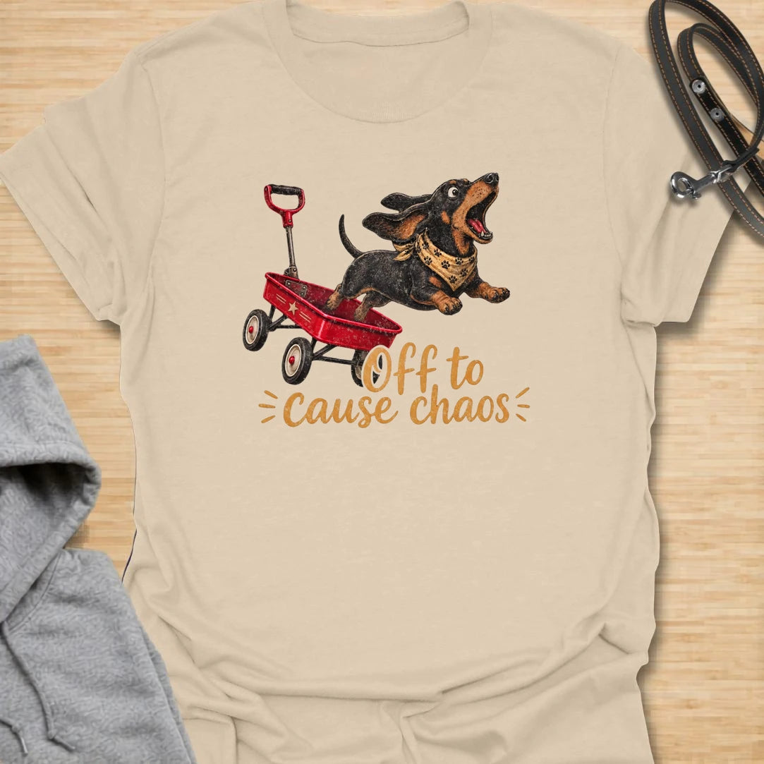 This Off To Cause Chaos t-shirt is made for dachshund lovers who know their little long dog is always ready for nonsense. Featuring a black and tan dachshund launching from a red wagon with a bandana and excited expression, this design has a fun action-filled dog-parent feel. Perfect for dachshund moms, dachshund dads, wiener dog fans, rescue dog lovers, and anyone whose doxie brings the chaos everywhere.