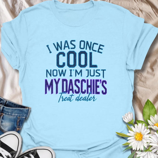 Life changes when a dachshund appoints you as the official treat dealer. This funny dachshund T-shirt is perfect for devoted daschie/doxie/daxie owners who know every snack request is urgent. A playful gift for dachshund moms, dads, and sausage dog lovers.