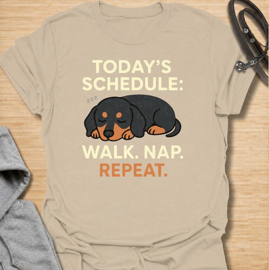 A funny dachshund T-shirt for anyone familiar with the very demanding daily routine of a sausage dog. Featuring the phrase “Today’s Schedule: Walk. Nap. Repeat.” with a sleepy dachshund illustration, this design captures the breed’s love of short adventures followed by serious rest. Perfect for dachshund moms, dachshund dads, wiener dog owners, and anyone whose dog has mastered the art of doing just enough. A playful everyday tee for fans of dachshund humor, lazy dog jokes, and breed-specific gifts.