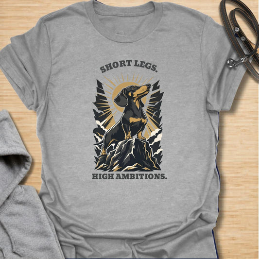 Short Legs High Ambitions t-shirt for dachshund lovers who know tiny legs never mean tiny confidence. This bold mountain-style design features a proud dachshund standing tall with dramatic vintage outdoor energy. A great gift for dachshund moms, dachshund dads, hikers, dog lovers, and anyone who loves a determined little sausage dog. Perfect for everyday wear, dog walks, casual weekends, or showing off big doxie attitude.