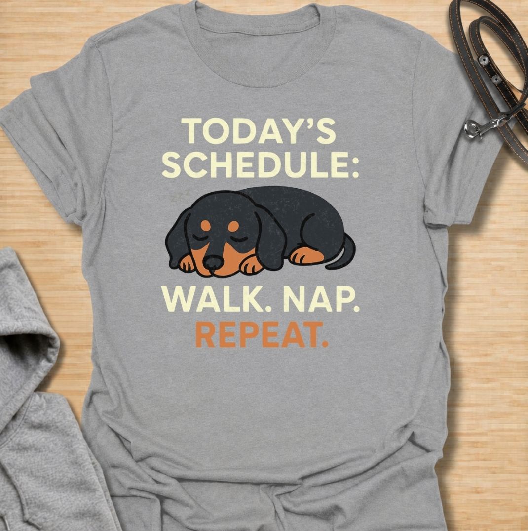 A funny dachshund T-shirt for anyone familiar with the very demanding daily routine of a sausage dog. Featuring the phrase “Today’s Schedule: Walk. Nap. Repeat.” with a sleepy dachshund illustration, this design captures the breed’s love of short adventures followed by serious rest. Perfect for dachshund moms, dachshund dads, wiener dog owners, and anyone whose dog has mastered the art of doing just enough. A playful everyday tee for fans of dachshund humor, lazy dog jokes, and breed-specific gifts.