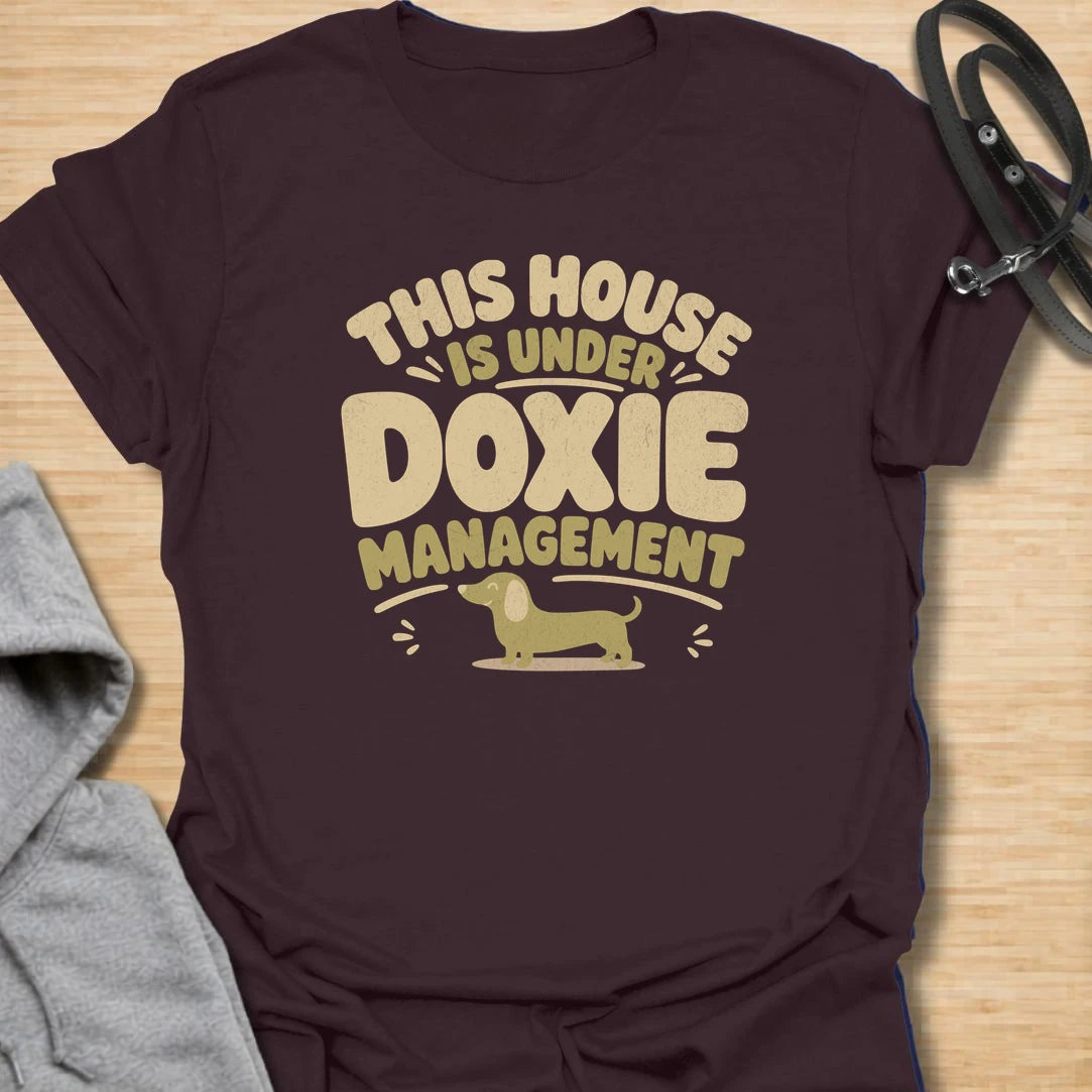 A funny dachshund T-shirt for homes where the smallest resident is clearly in charge. The cheerful retro lettering and little sausage dog perfectly capture life under strict doxie management. A fun gift for dachshund moms, dachshund dads, new puppy owners, and anyone whose dog runs the household.
