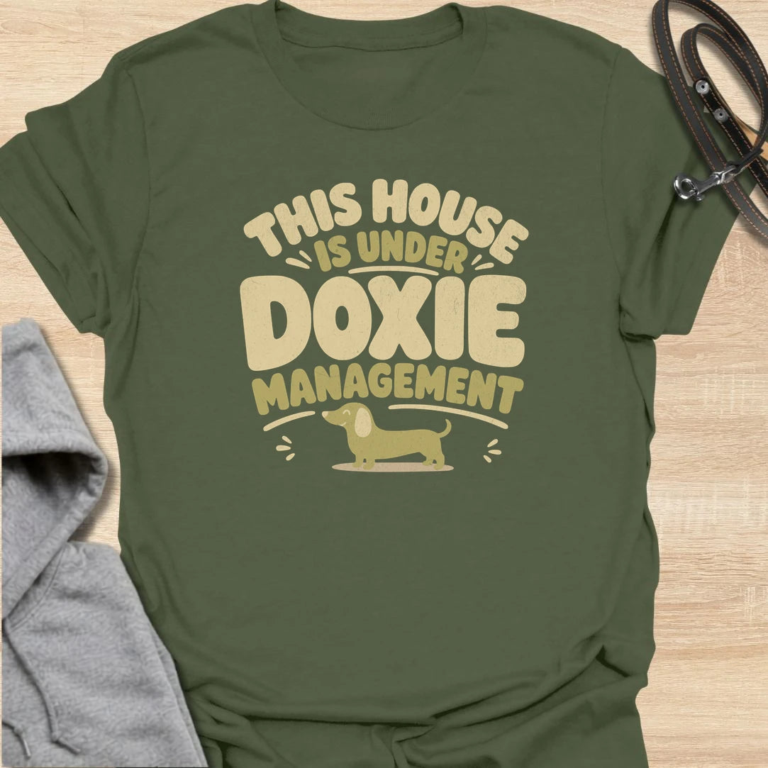 A funny dachshund T-shirt for homes where the smallest resident is clearly in charge. The cheerful retro lettering and little sausage dog perfectly capture life under strict doxie management. A fun gift for dachshund moms, dachshund dads, new puppy owners, and anyone whose dog runs the household.