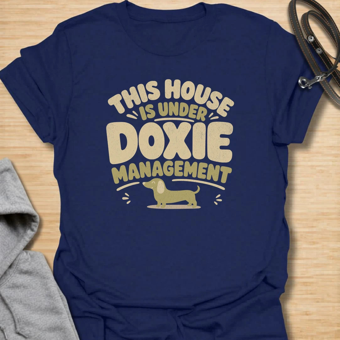 A funny dachshund T-shirt for homes where the smallest resident is clearly in charge. The cheerful retro lettering and little sausage dog perfectly capture life under strict doxie management. A fun gift for dachshund moms, dachshund dads, new puppy owners, and anyone whose dog runs the household.