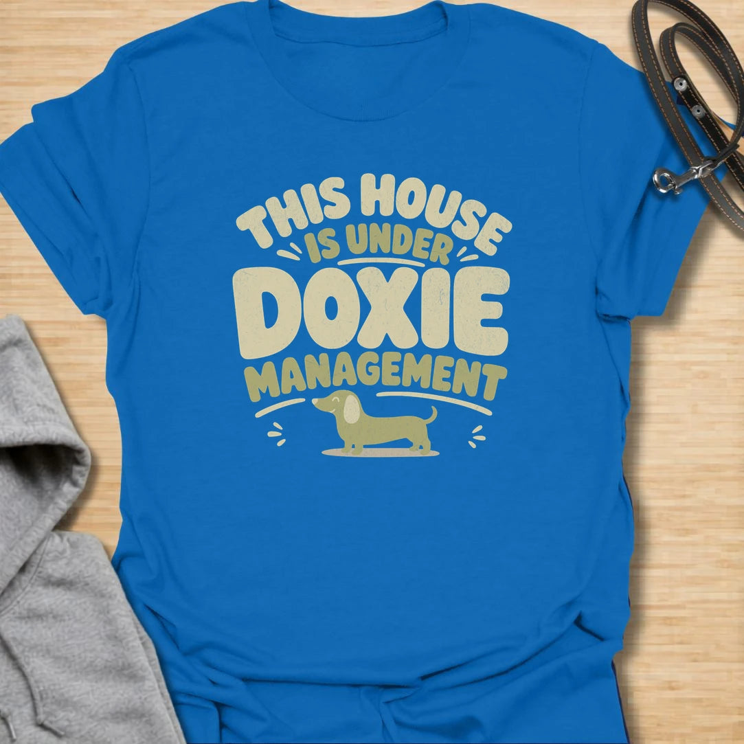 A funny dachshund T-shirt for homes where the smallest resident is clearly in charge. The cheerful retro lettering and little sausage dog perfectly capture life under strict doxie management. A fun gift for dachshund moms, dachshund dads, new puppy owners, and anyone whose dog runs the household.