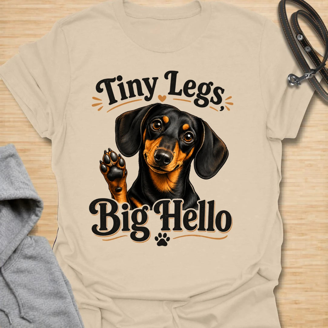 This Tiny Legs Big Hello t-shirt is made for dachshund lovers who know their little long dog can make a very big entrance. Featuring a cute black and tan dachshund waving a paw, playful retro lettering, and small heart and paw details, this design has a friendly, funny dog-lover feel. Perfect for dachshund moms, dachshund dads, wiener dog fans, doxie owners, sausage dog lovers, and anyone whose tiny-legged best friend is always ready to say hello. Sand