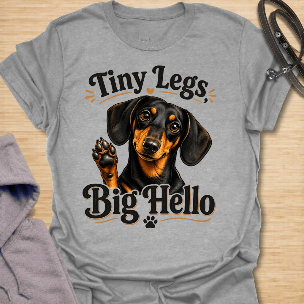 This Tiny Legs Big Hello t-shirt is made for dachshund lovers who know their little long dog can make a very big entrance. Featuring a cute black and tan dachshund waving a paw, playful retro lettering, and small heart and paw details, this design has a friendly, funny dog-lover feel. Perfect for dachshund moms, dachshund dads, wiener dog fans, doxie owners, sausage dog lovers, and anyone whose tiny-legged best friend is always ready to say hello. Sport Grey