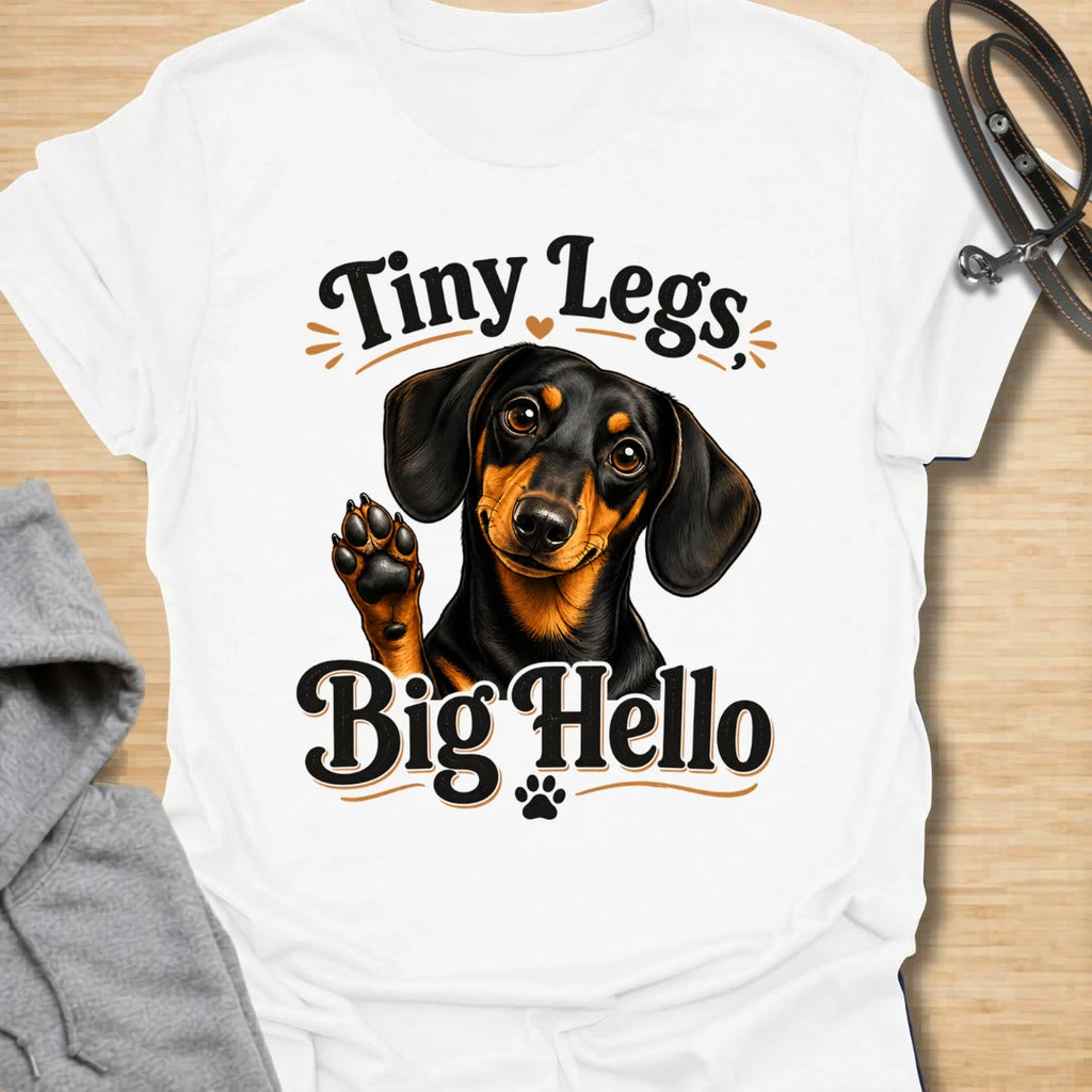 This Tiny Legs Big Hello t-shirt is made for dachshund lovers who know their little long dog can make a very big entrance. Featuring a cute black and tan dachshund waving a paw, playful retro lettering, and small heart and paw details, this design has a friendly, funny dog-lover feel. Perfect for dachshund moms, dachshund dads, wiener dog fans, doxie owners, sausage dog lovers, and anyone whose tiny-legged best friend is always ready to say hello. White